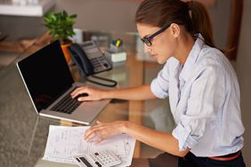 Woman looking at financial papers next to laptop and calculator