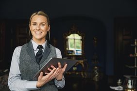 A concierge standing inside a hotel, holding a digital tablet, ready to help