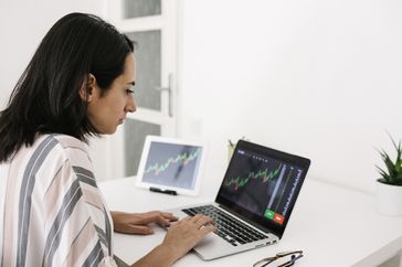 Young trader woman reading financial stock market analysis on laptop at home 