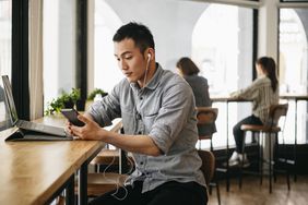 Man with laptop uses earbuds and cellphone in cafe