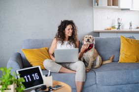 Woman sitting on couch with dog, working on laptop 