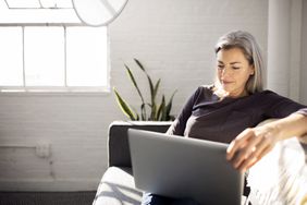 woman in black shirt with grey hair sitting on couch doing work