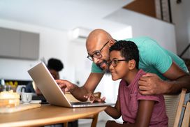 A child and parent look at a laptop.