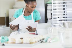 Female baker consults bills and digital tablet in kitchen