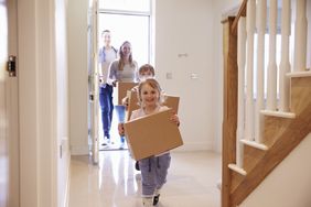 Couple with two children carrying boxes through front door of new home