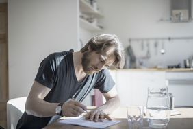 A person writes on a sheet of paper in a kitchen.