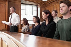 Several people sit along a bench in a courtroom.