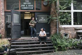 Two business owners standing outside indie coffee shop with door open