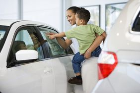 A customer holding a toddler looks at a Monroney sticker on a new car.