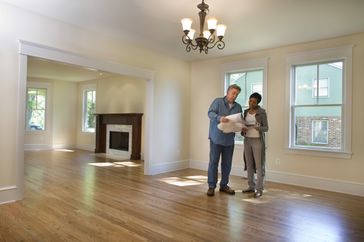 A woman and a man stand in an empty home looking over plans. 